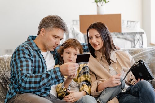 Free Happy family sitting on couch looking at instant photo in their new home. Stock Photo