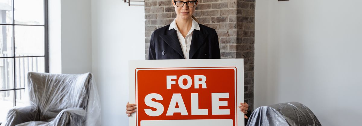 A woman beside a For Sale sign in a home