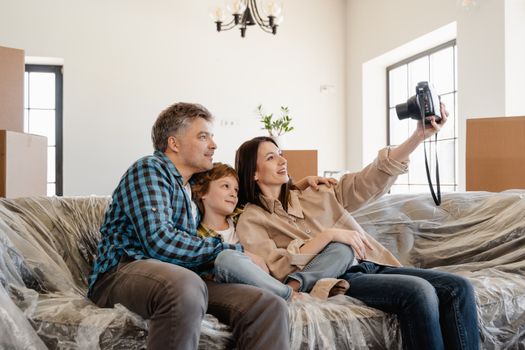 Family taking a selfie on moving day, sitting on a couch amidst packed boxes.