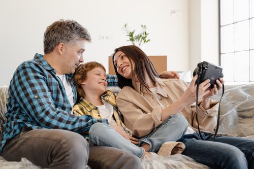 Free Happy family sitting on sofa, enjoying a Polaroid camera at home. Stock Photo