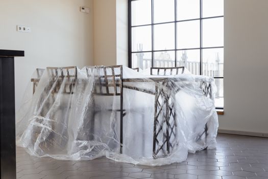 Dining chairs and table covered in plastic, a new home interior ready for moving in.