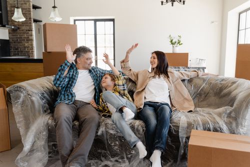 Free A cheerful family sitting on a couch amidst moving boxes, celebrating their new home. Stock Photo