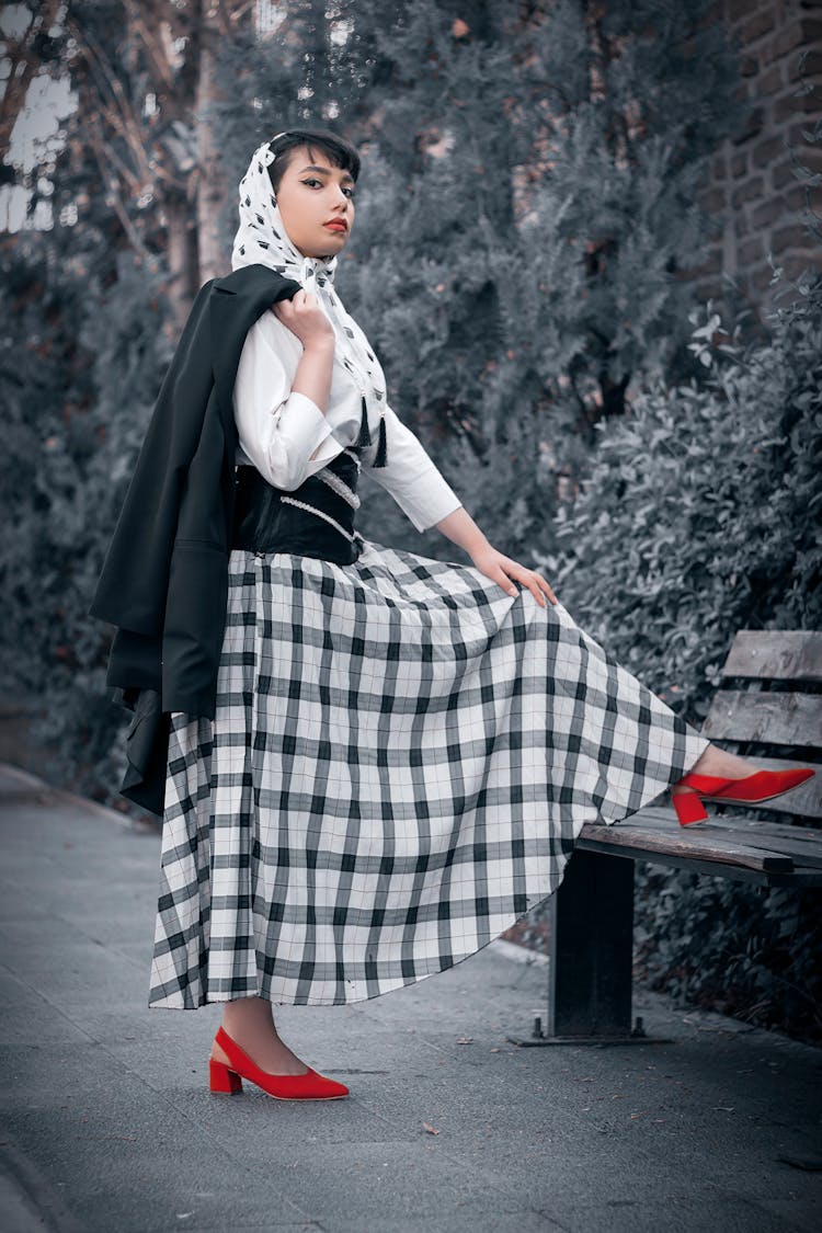 
A Woman Wearing A Plaid Skirt And A Headscarf Holding Her Blazer