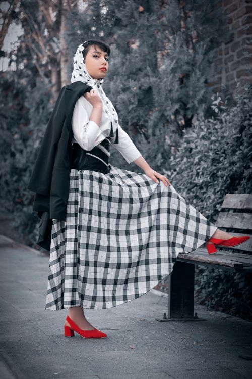 Free Fashionable woman poses in a black and white plaid skirt with red heels in an urban setting. Stock Photo