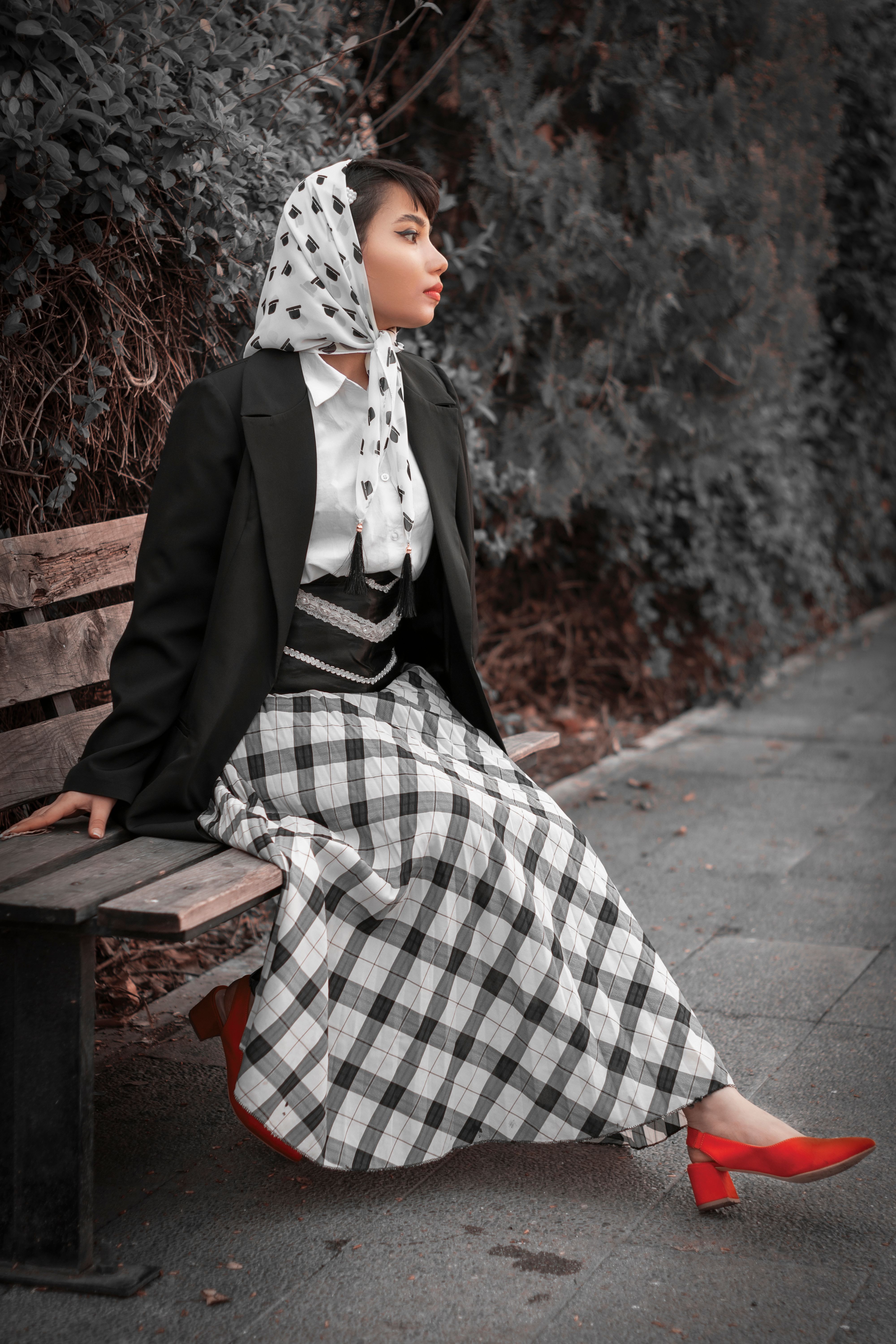 Fashionable woman in black blazer and headscarf, sitting outdoors on a bench in Tehran.