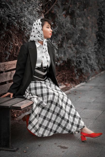 Fashionable woman in black blazer and headscarf, sitting outdoors on a bench in Tehran.