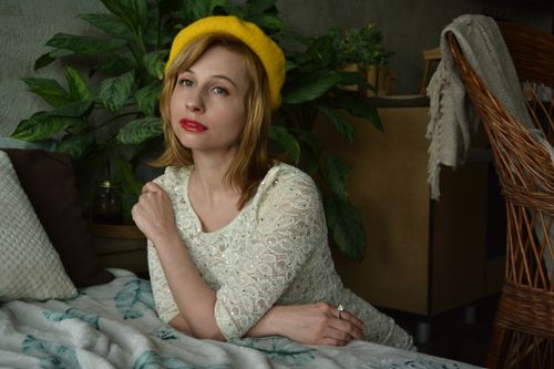 Free Medium shot of thoughtful blond haired lady in stylish old fashioned outfit touching shoulder and leaning on soft sofa decorated with pillows Stock Photo
