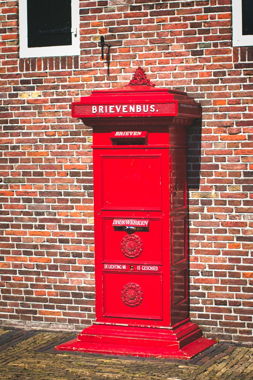 Classic rode Nederlandse brievenbus tegen een gemeleerde bakstenen muur, in Volendam, Nederland.