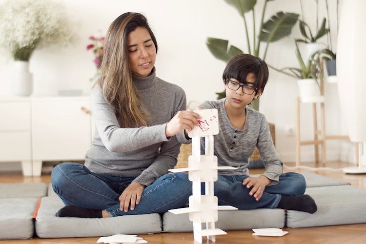 A Mother And Son Sitting On Cushions On The Floor While Playing Paper Tower