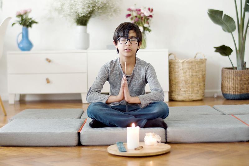 A young boy meditating on cushions at home beside a lit candle