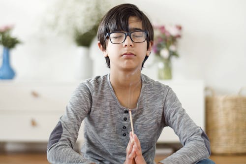 Boy in Eyeglasses Sitting with his Hands Clasped and Eyes Closed