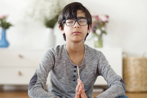 Free Boy in Eyeglasses Sitting with his Hands Clasped and Eyes Closed Stock Photo