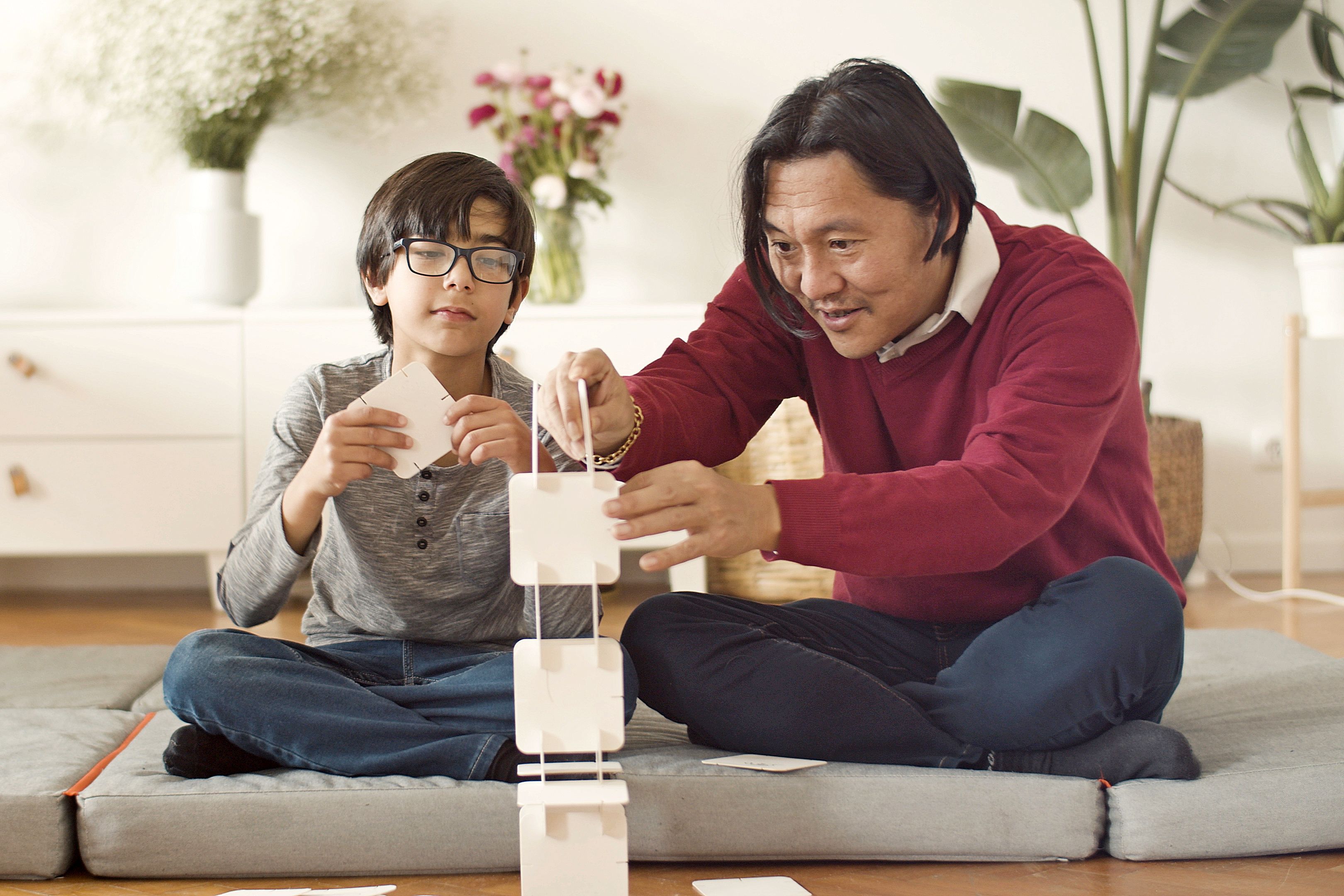 A father and child building a card tower together during a cooperative problem-solving activity at home
