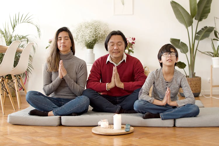 A Family Sitting On Cushions On The Floor While Meditating Together