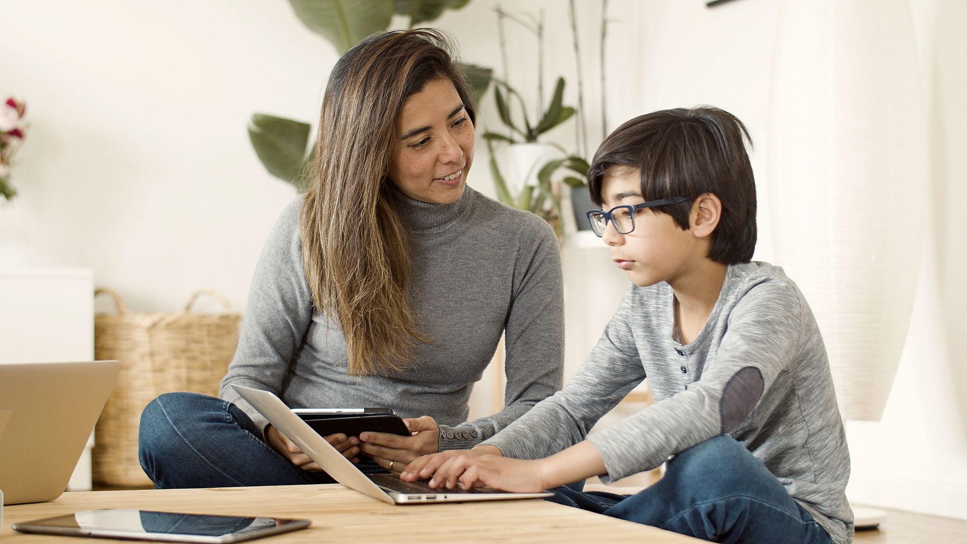 A mother and her son using a laptop and tablet together in a cozy home setting.