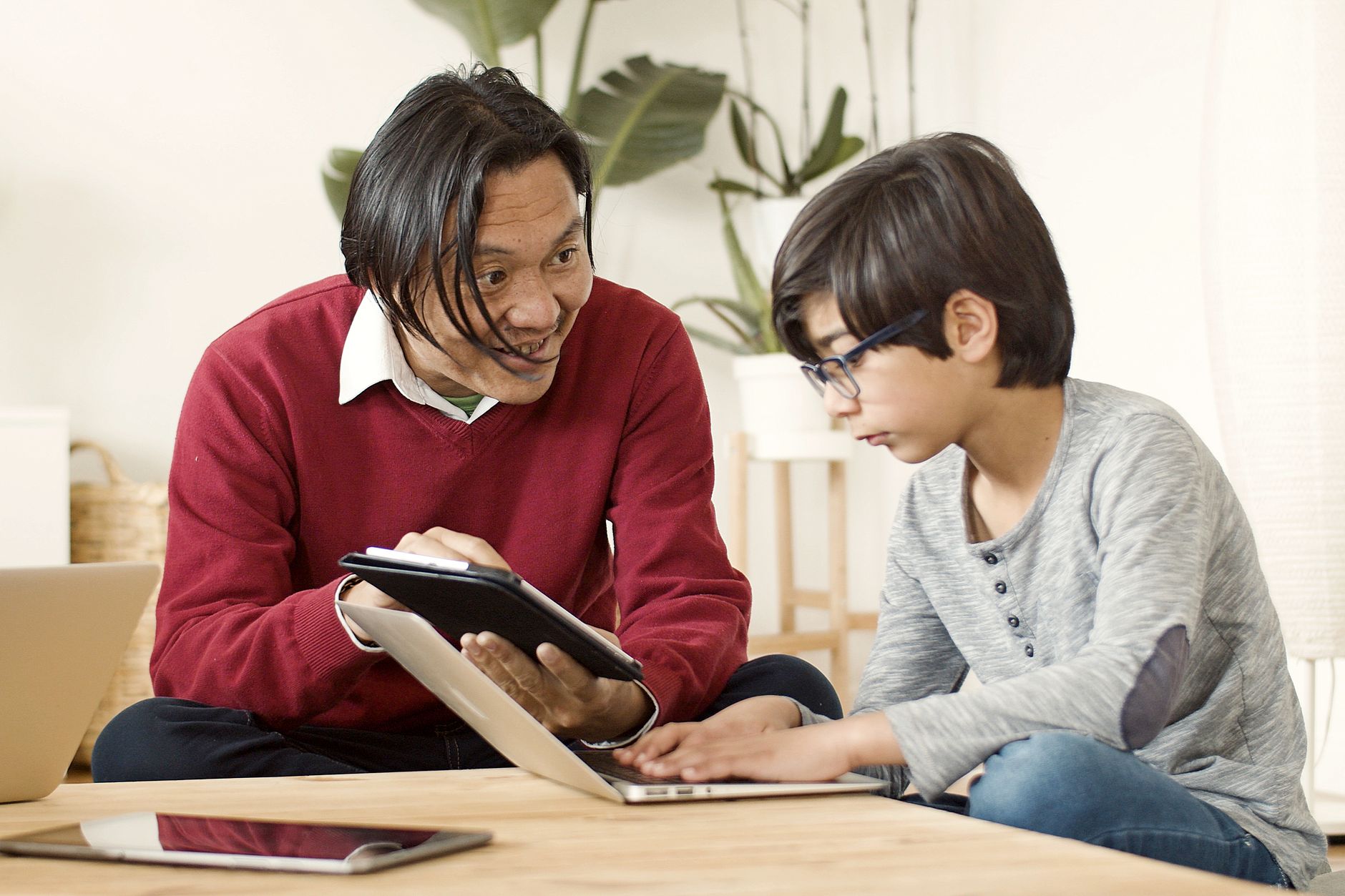 Asian father and son bonding time with laptop and tablet, learning and interacting at home.