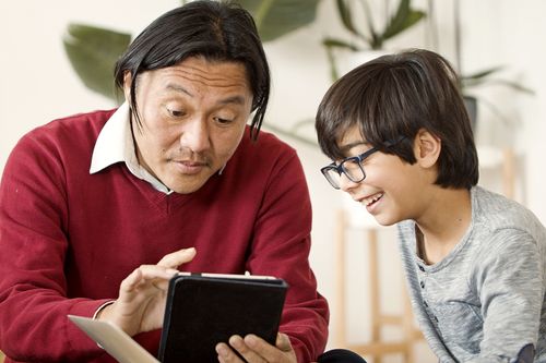 Free Asian father and child using tablet together in cozy indoor setting. Stock Photo