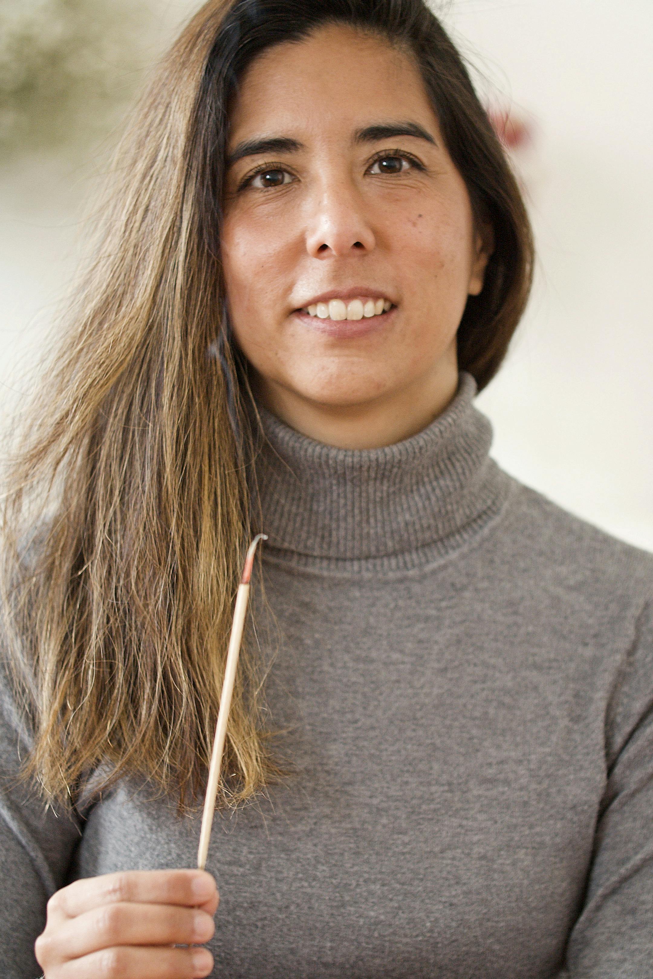 Close-up portrait of a smiling woman in a gray sweater holding an incense stick, conveying warmth and serenity.