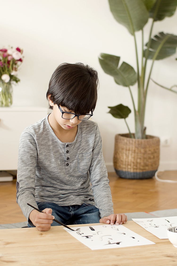 A Young Boy In Gray Sweater Drawing On White Papers