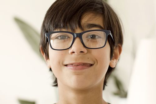 Free A close-up of a smiling young boy wearing eyeglasses indoors, captured in a natural light setting. Stock Photo