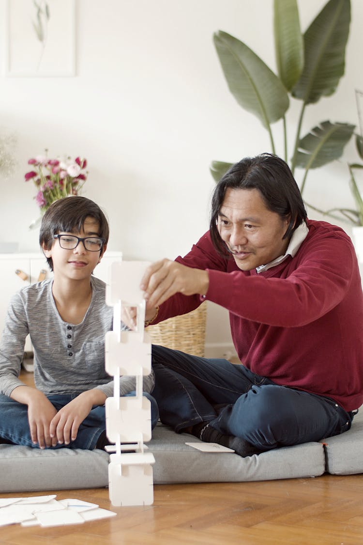 Father And Son Sitting On Floor And Building From Cards