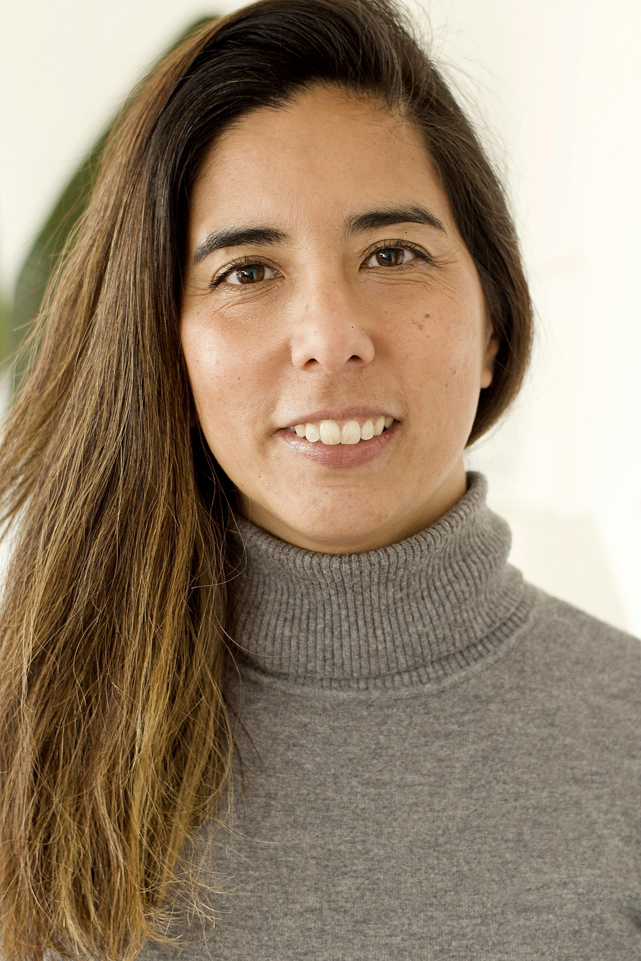 Close-up portrait of a smiling woman in a gray turtleneck sweater with a warm and inviting expression.