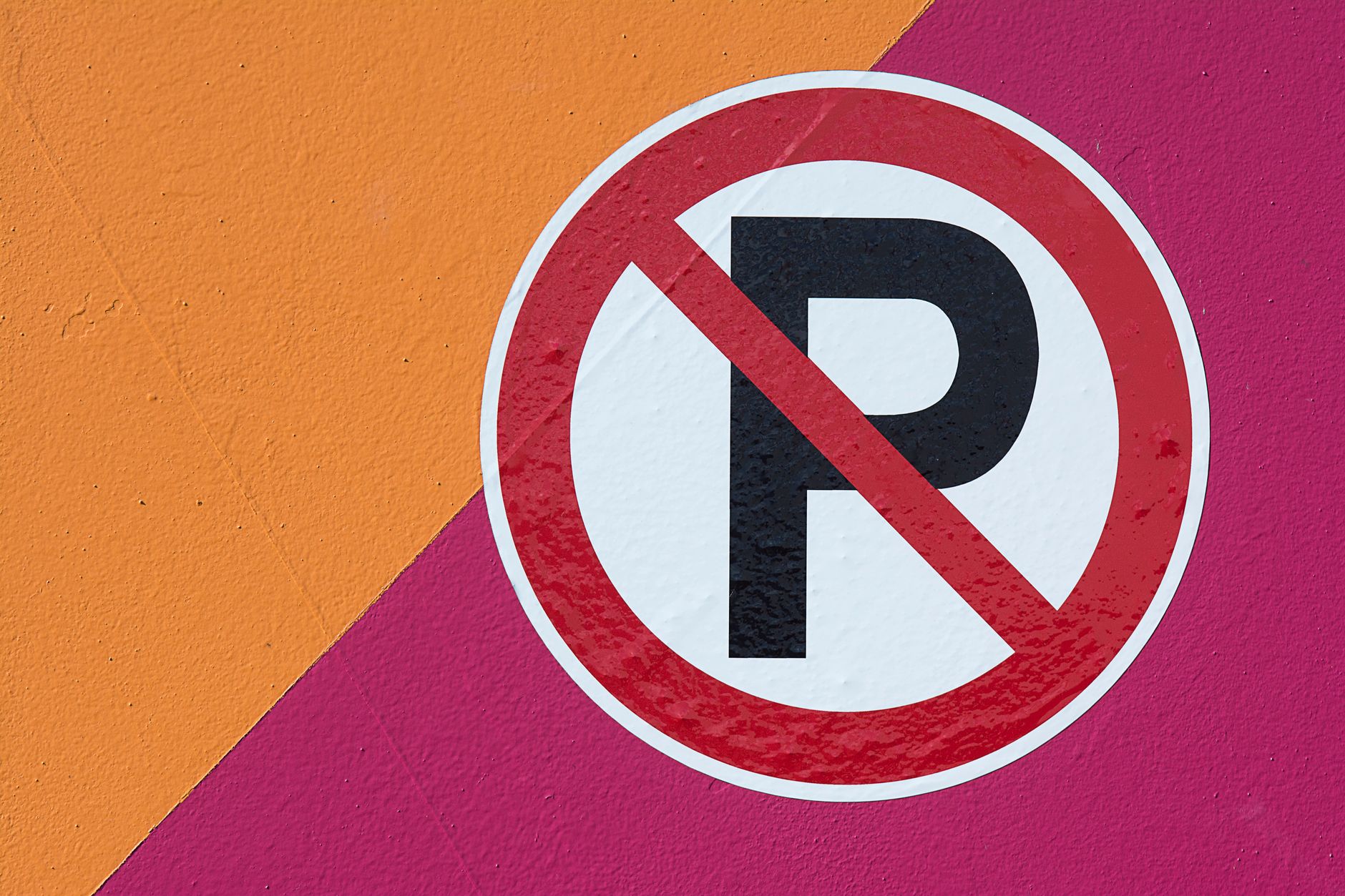 A no parking sign displayed on a vibrant orange and pink angular background wall.
