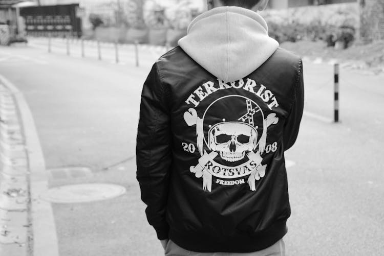 Back View Of A Man Walking On A City Street Wearing A Jacket With Skull Graphic On The Back 