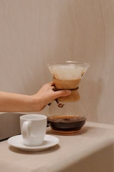 A hand pours fresh coffee from a dripper into a ceramic cup, creating a cozy indoor atmosphere.