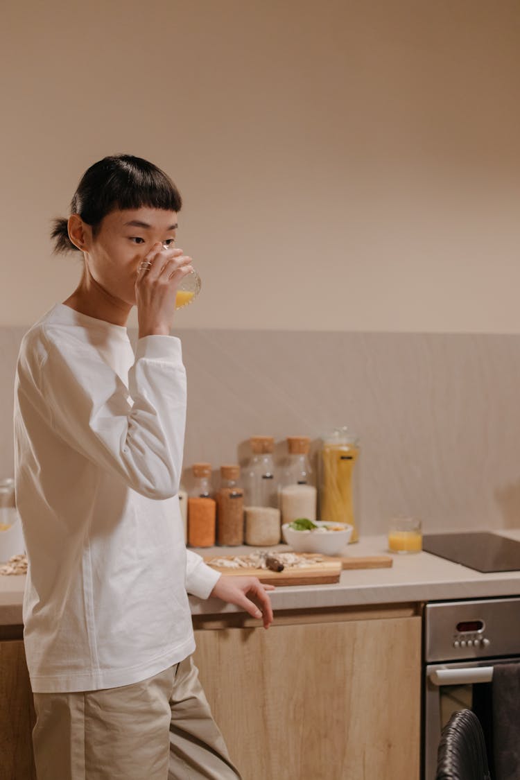 Young Asian Woman Drinking Fresh Orange Juice In Kitchen