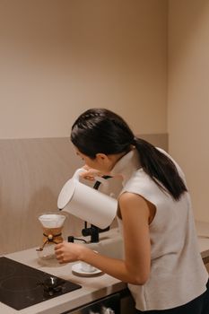 A woman preparing pour-over coffee in a modern kitchen, showing careful attention to detail.