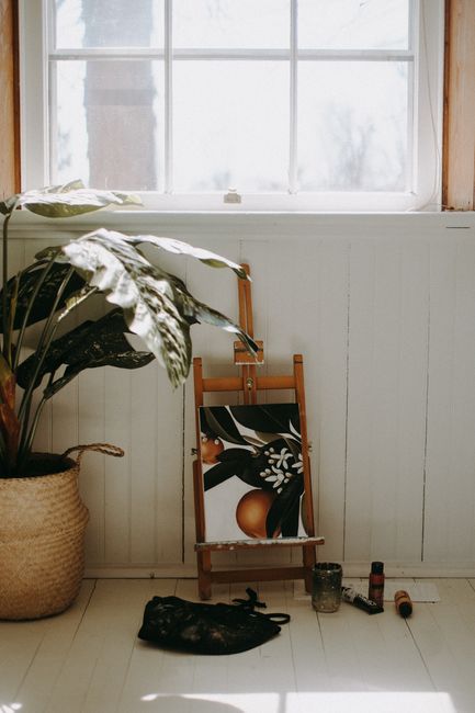 A Monstera plant and painting on a wooden easel beside a bright window, evoking a cozy artistic atmosphere.
