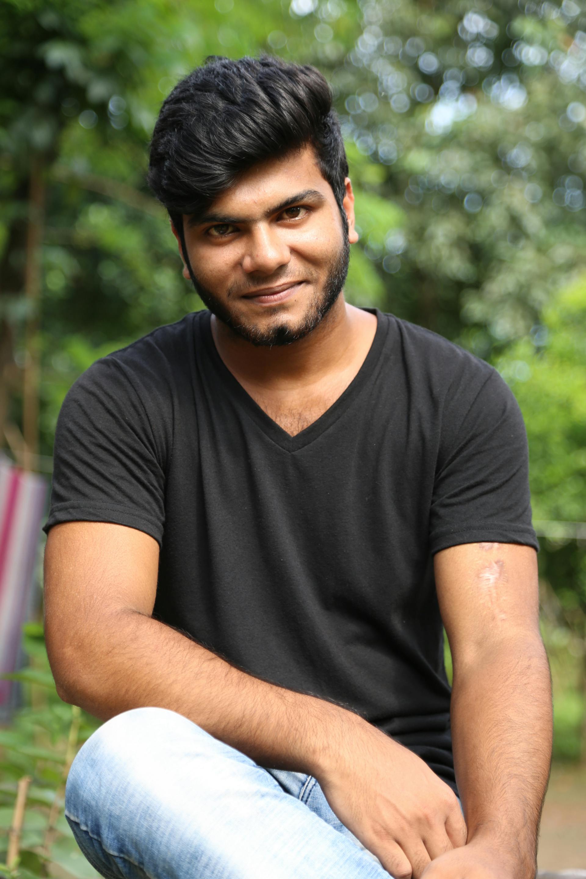 Smiling man with beard in black shirt poses in lush green park.