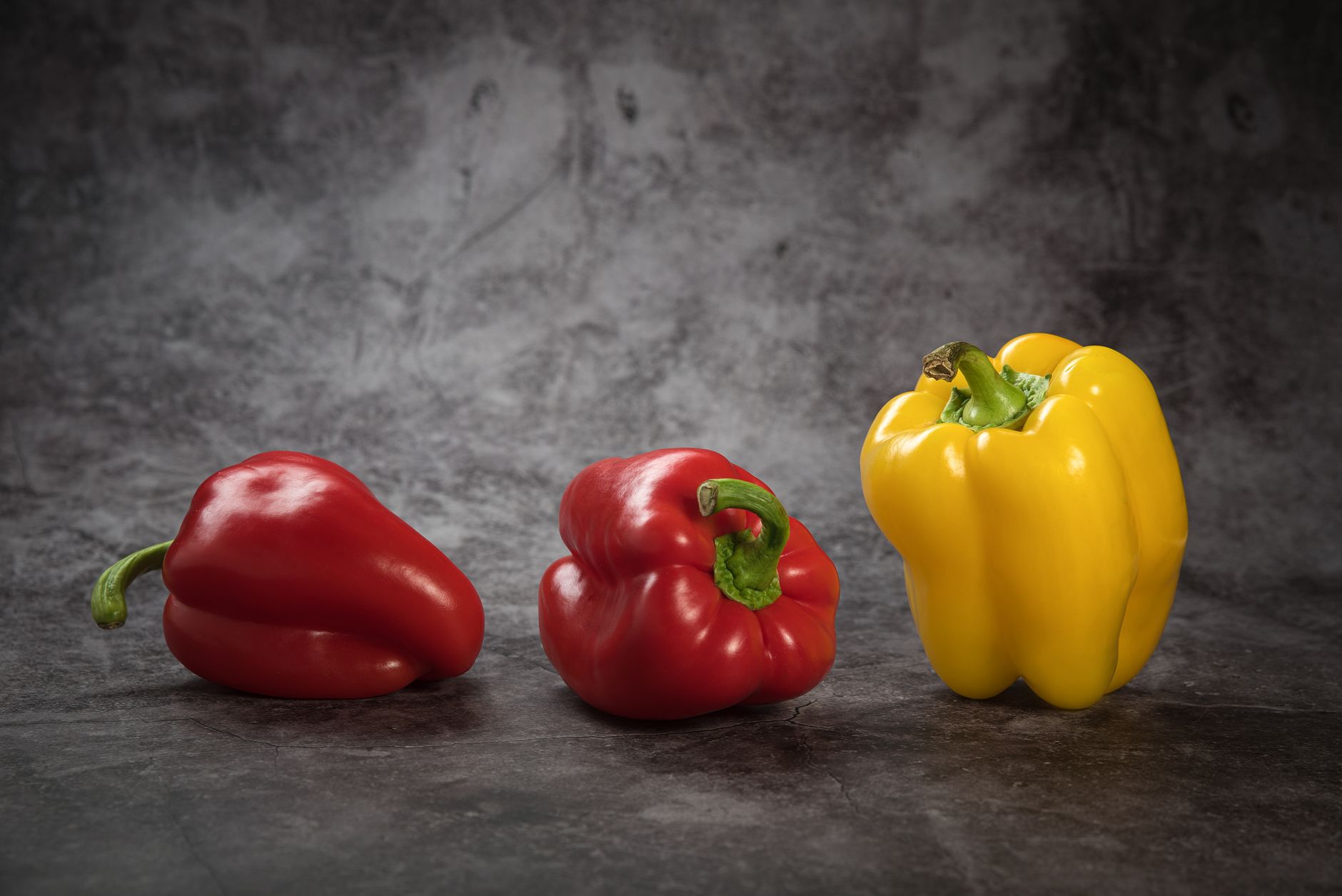 Colorful red and yellow bell peppers arranged on a textured dark background in a still life composition.