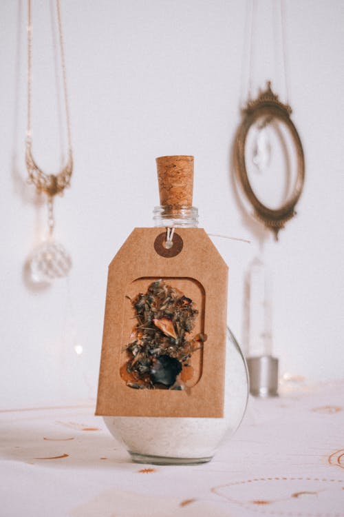 Simple vintage glass bottle full of white aromatic bath salt near hanging shimmering pendant on blurred background