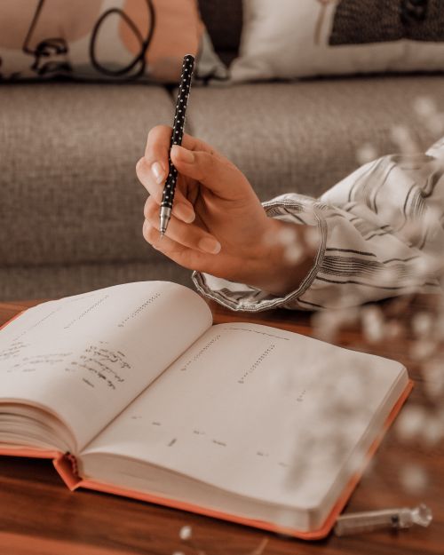 Free Crop unrecognizable student wearing casual clothes sitting at desk and taking notes in schedule with pen in organizer at daytime Stock Photo