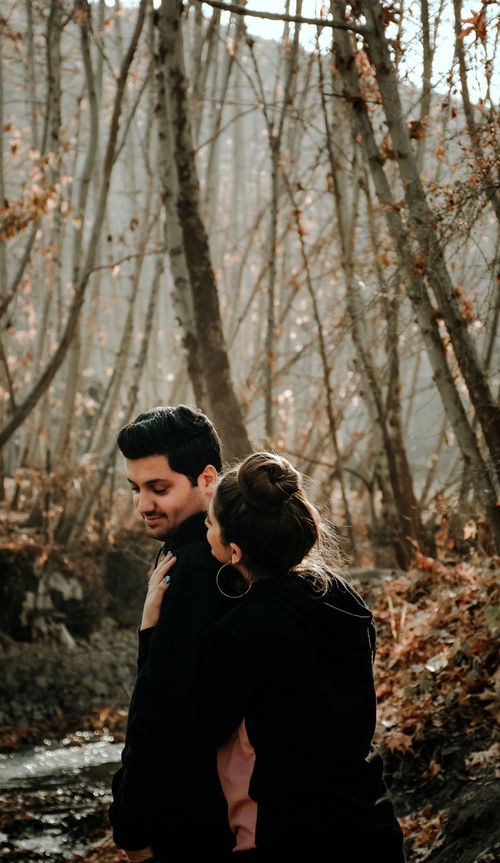 Free Side view of female embracing happy Hispanic male from back while standing on romantic walk in woods in fall in daylight Stock Photo