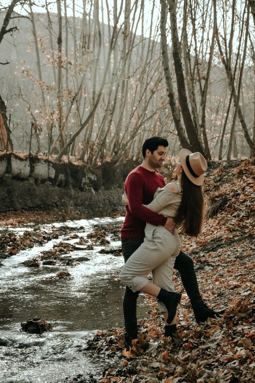 Free Stylish romantic Hispanic couple in warm clothes flirting and cuddling while standing close in forest in fall season in daytime Stock Photo