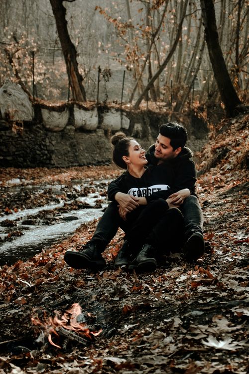 Free Full body of Hispanic couple in cozy outfits laughing and looking at each other while hugging near bonfire in park in daylight Stock Photo