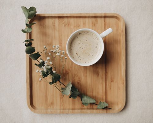 Free A ceramic mug of coffee on a wooden tray adorned with eucalyptus leaves and flowers. Stock Photo