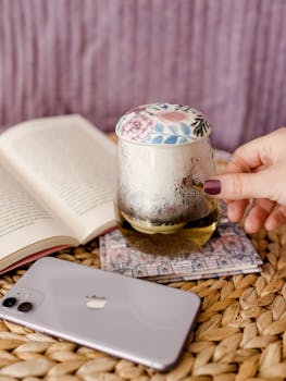 A relaxing setting with a hand holding herbal tea beside an open book and smartphone.