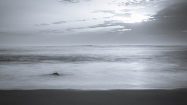 A serene monochrome ocean view at dusk with calm waves and cloudy sky.