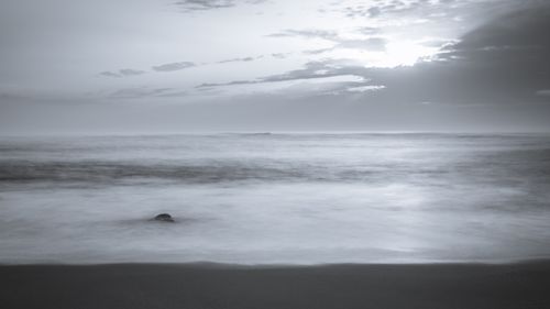 Free A serene monochrome ocean view at dusk with calm waves and cloudy sky. Stock Photo