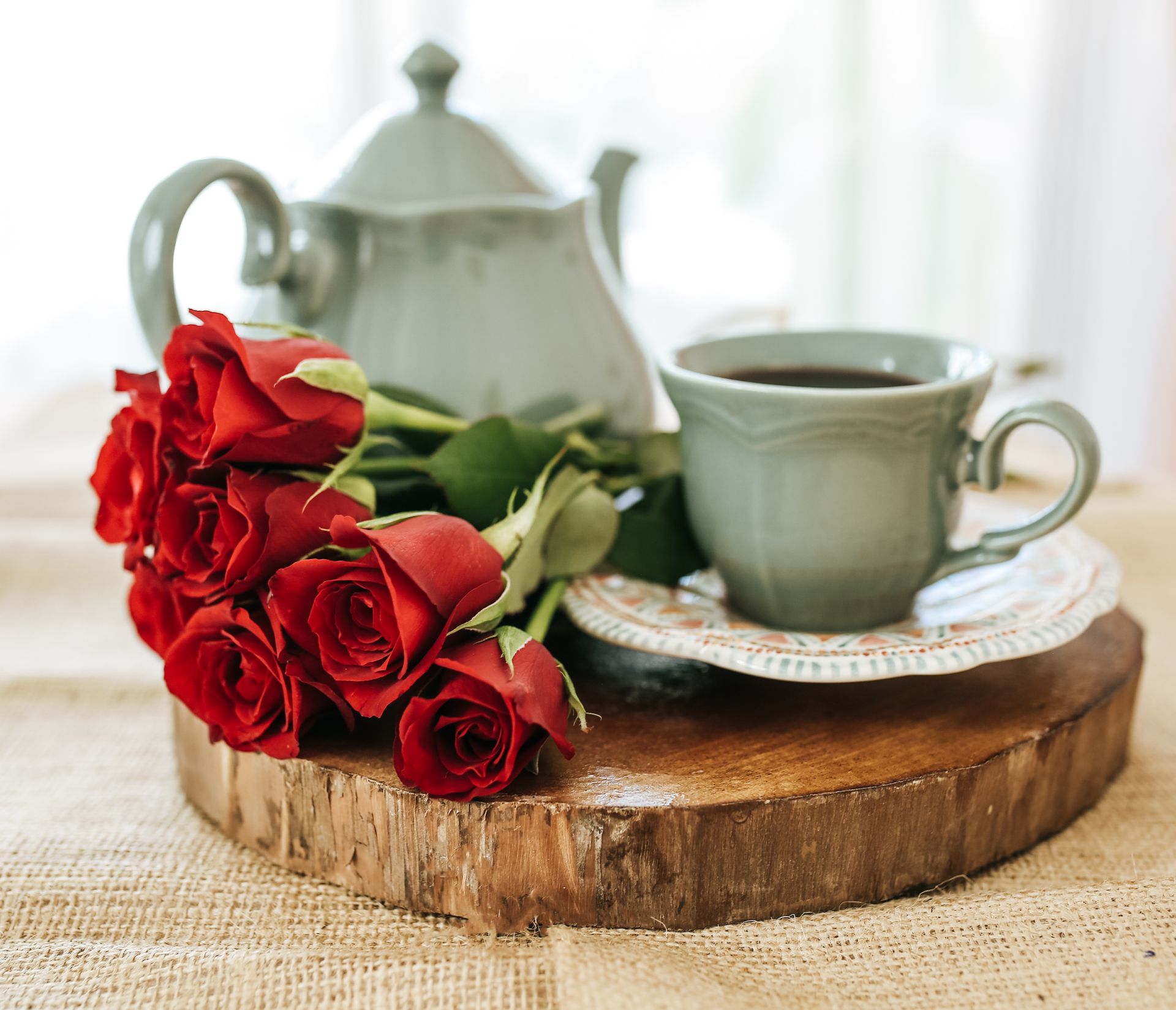 A charming indoor tea setup with red roses and porcelain teapot on a rustic wood board.