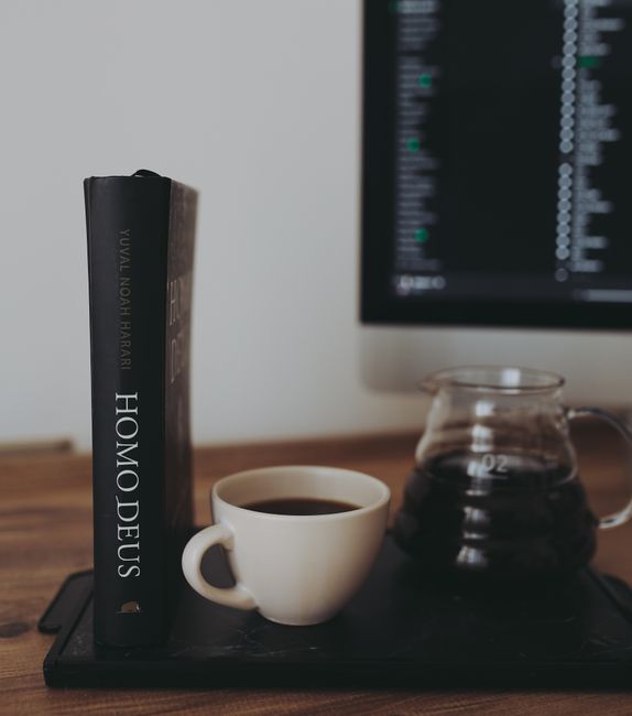 Tray with cup and pot with glass pot of freshly brewed coffee near book placed on table near computer in room