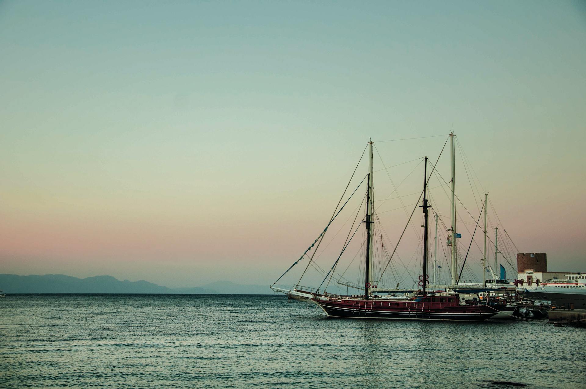 A tranquil sunset over Rhodes harbor featuring a majestic ship silhouette.
