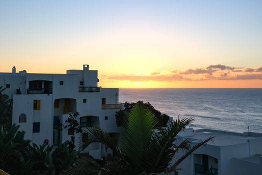 Stunning view of modern apartment by the ocean at sunrise, featuring clear skies and palm trees.