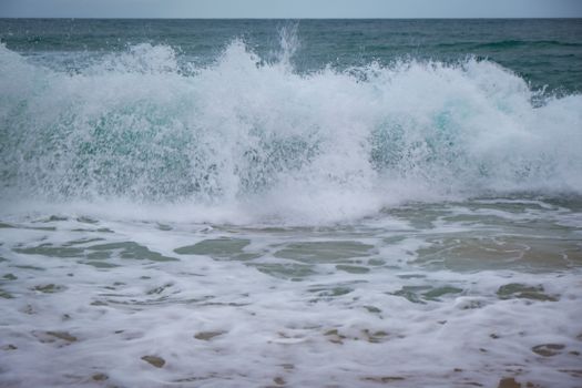 Dynamic capture of ocean waves crashing on a sandy beach, creating a splash of white foam.