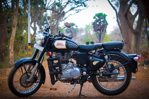 Free A classic Royal Enfield motorcycle parked on a dirt path surrounded by trees. Stock Photo