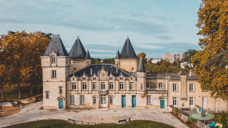 Vue aérienne majestueuse d'un château historique à Bordeaux, entouré d'arbres d'automne.